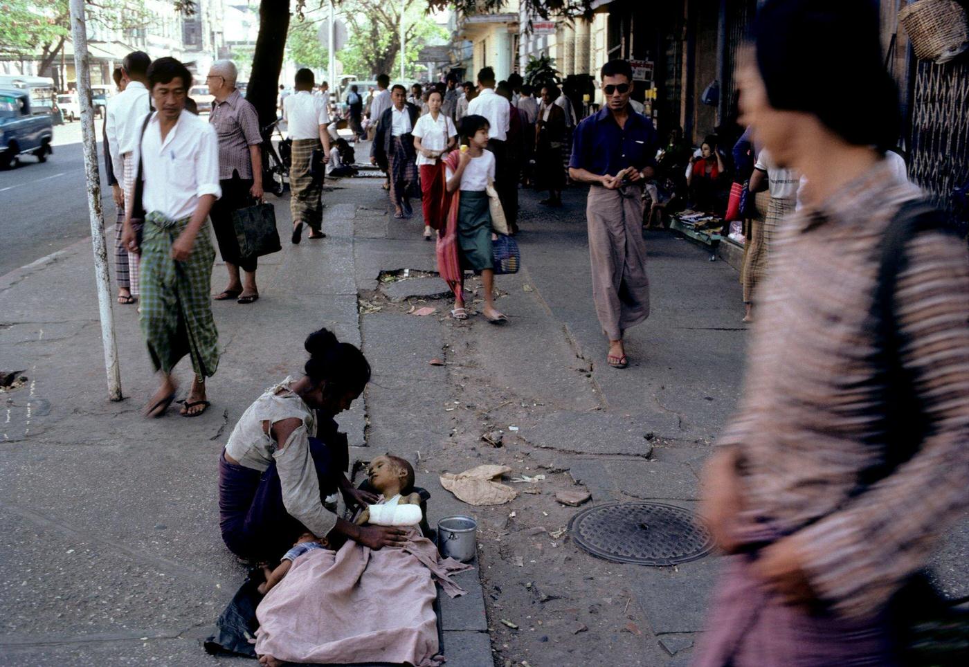 #1 Poverty-Stricken Mother Comforts Malnourished Injured Child While Begging in Rangoon, Burma, 1985