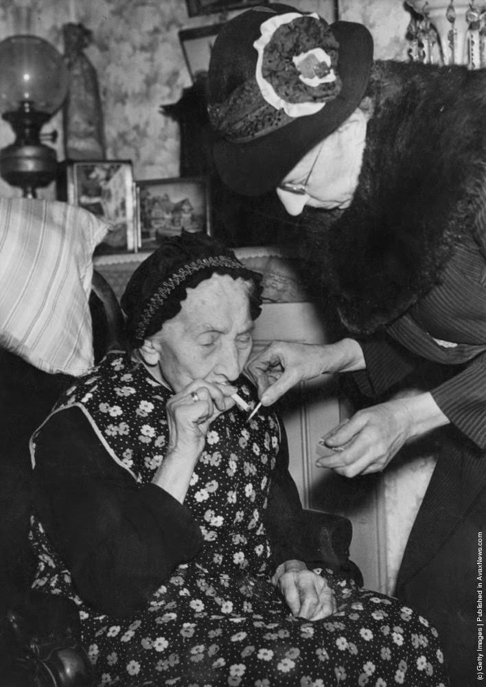 #16 75 year-old Mary Parish lights a cigarette for her 101 year-old mother, Mary Ann Parish, at their home in Walworth, London, 14th February 1946.