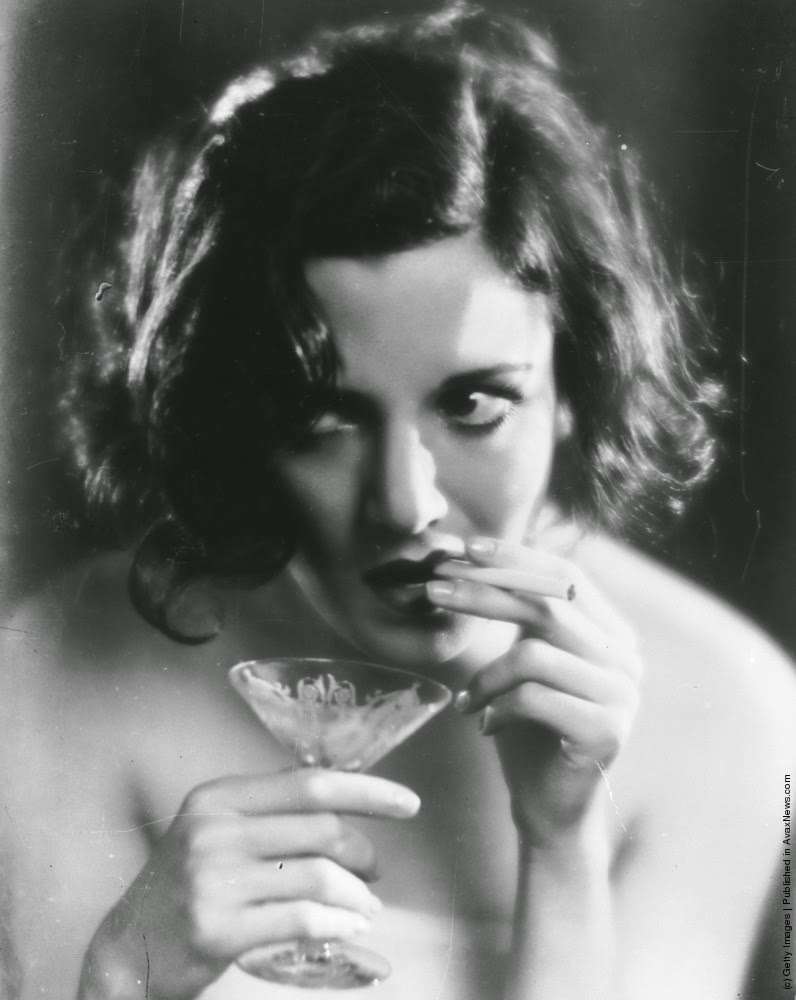 #17 A woman smokes a cigarette while holding a cocktail glass in the other hand, 1930