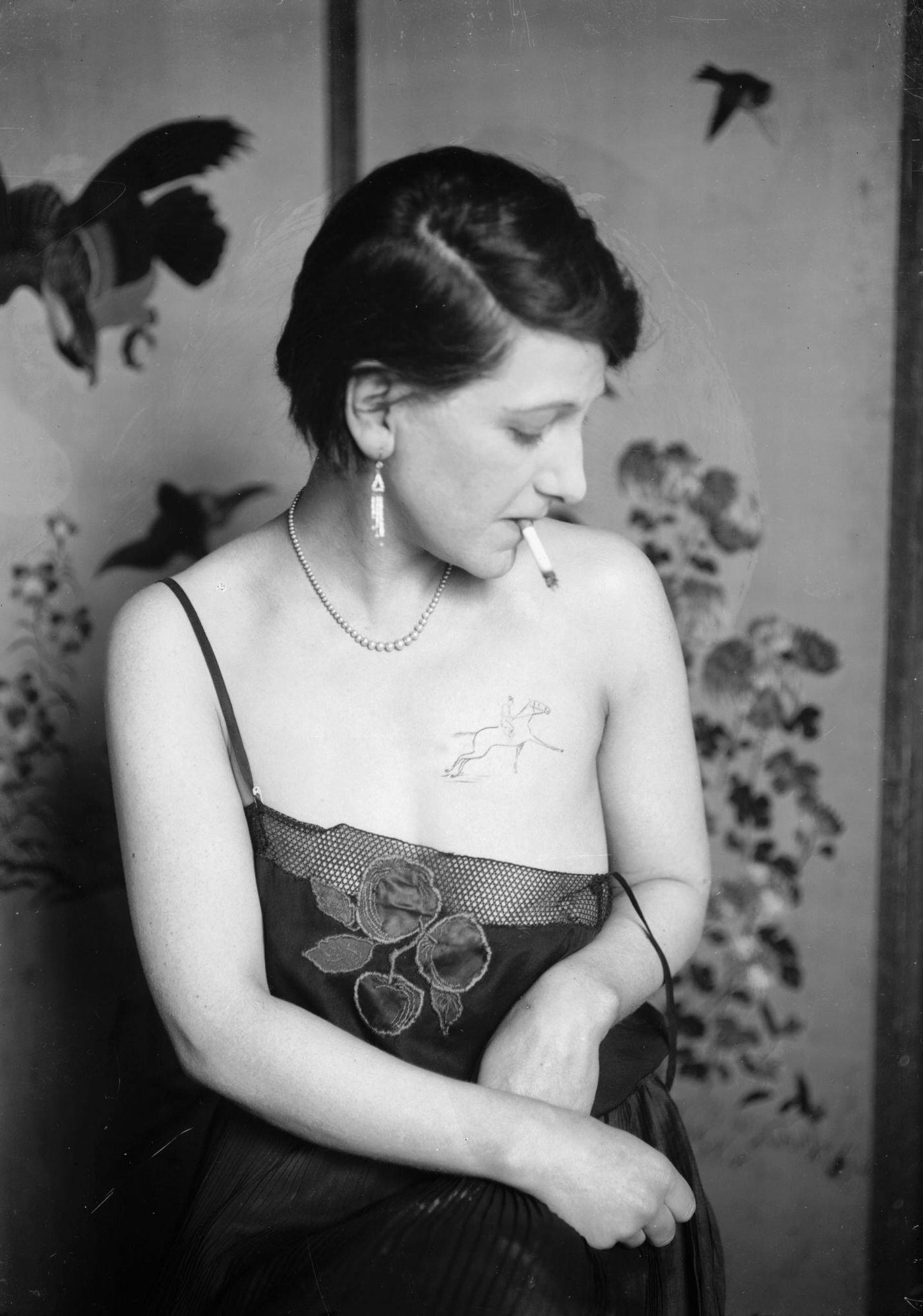 #5 A young woman has a tattoo of a horse and jockey on her breast, visible above an underslip, 1930.