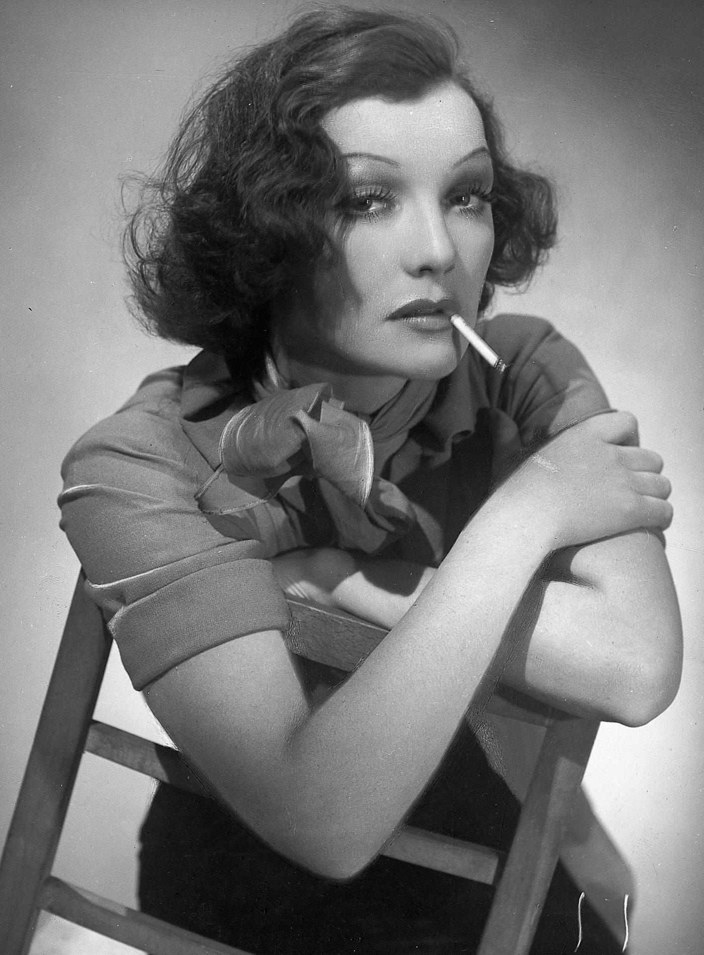 #29 Brunette woman, rouged strongly, sits on a chair and smokes a cigarette, 1930.