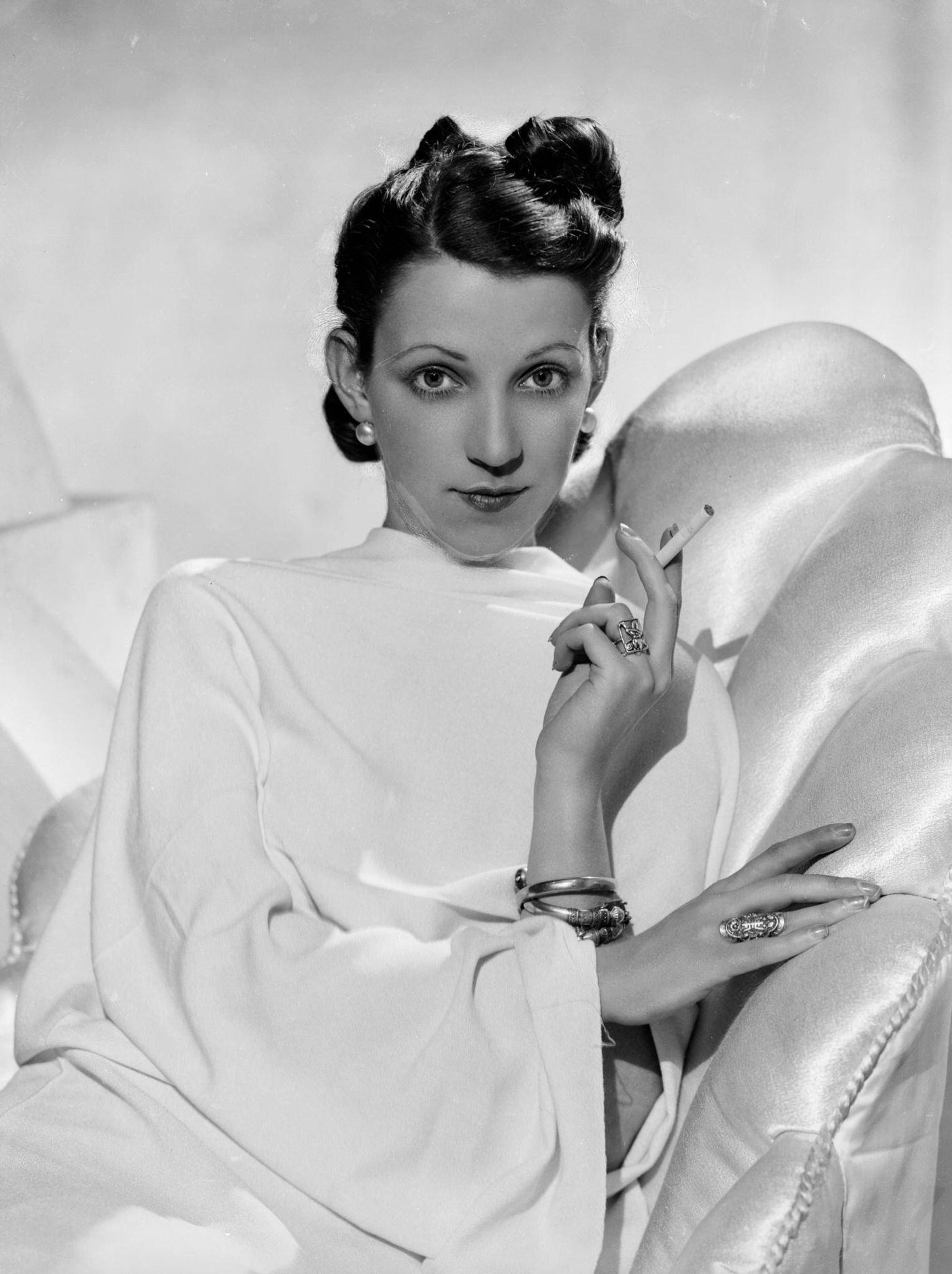 #54 A glamorous fashion model wearing a vestal gown and resting on a sumptuous recliner, 1935