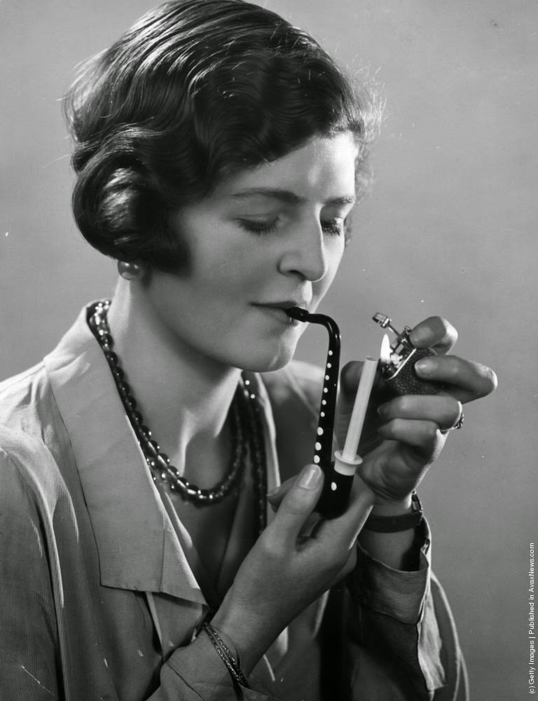 #13 A lady is pictured lighting her cigarette now held in a novelty cigarette holder in the shape of a musical instrument, 1932