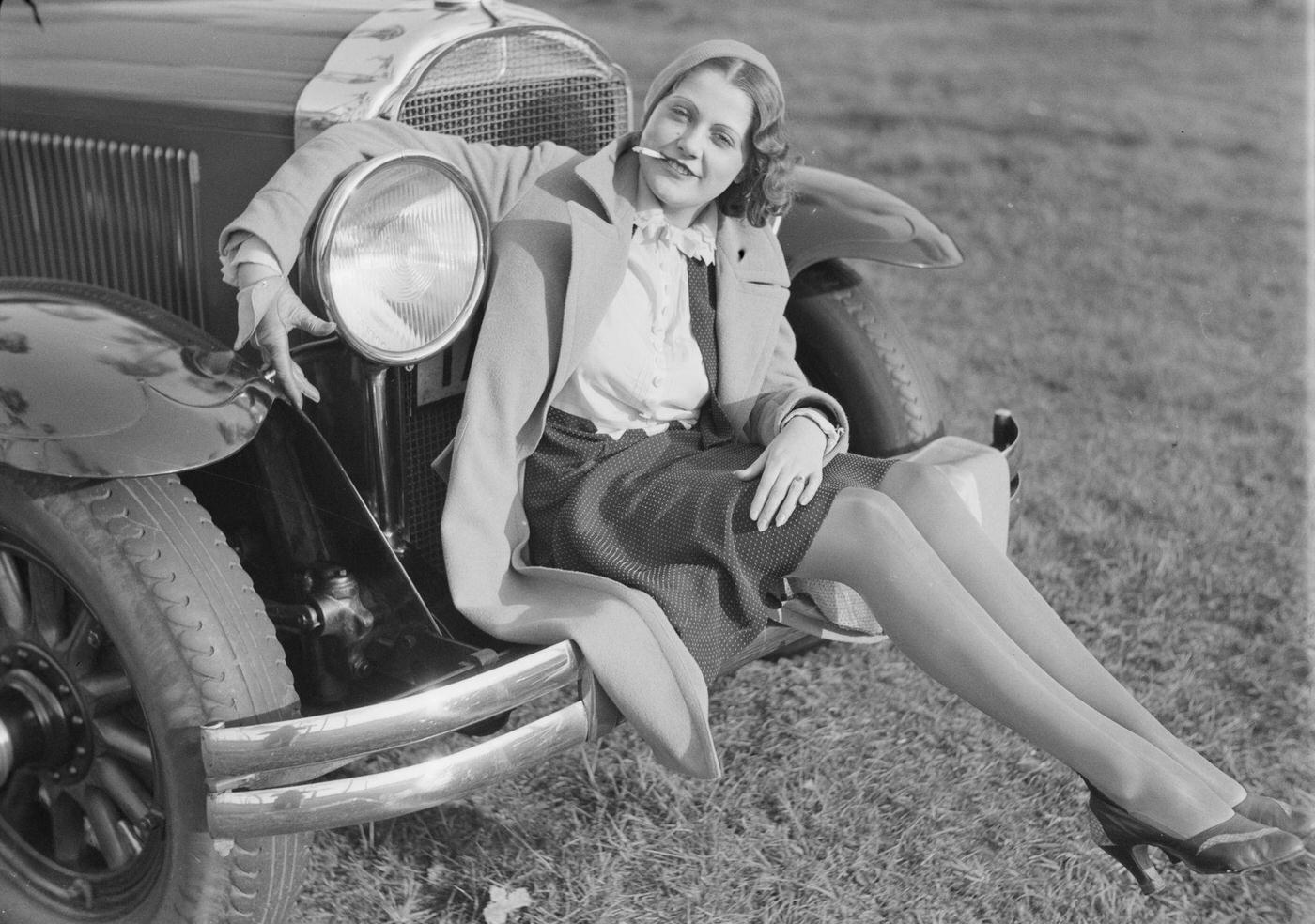 #78 Young woman sitting on the bumper of a car, smoking a cigarette, 1930