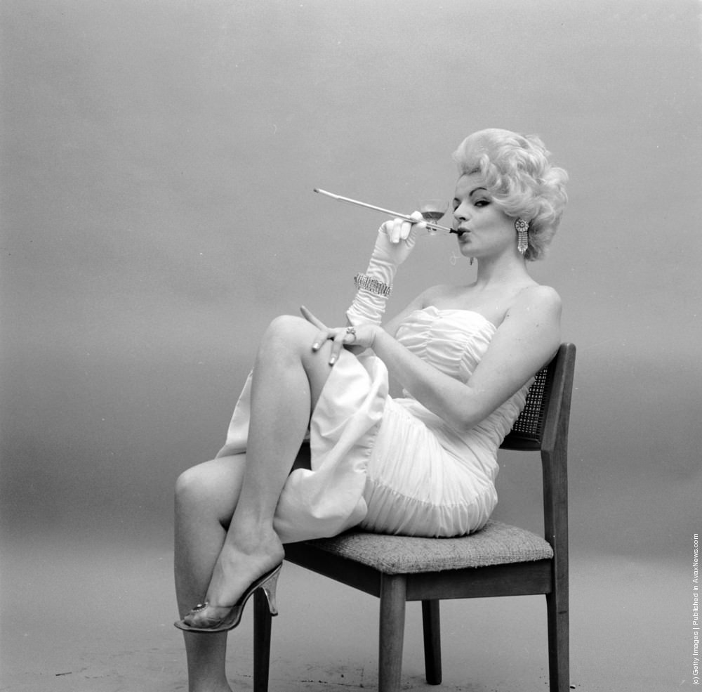 #12 Model Bonnie Sharie uses a long cigarette holder with an unusual wine glass attachment, circa 1955.