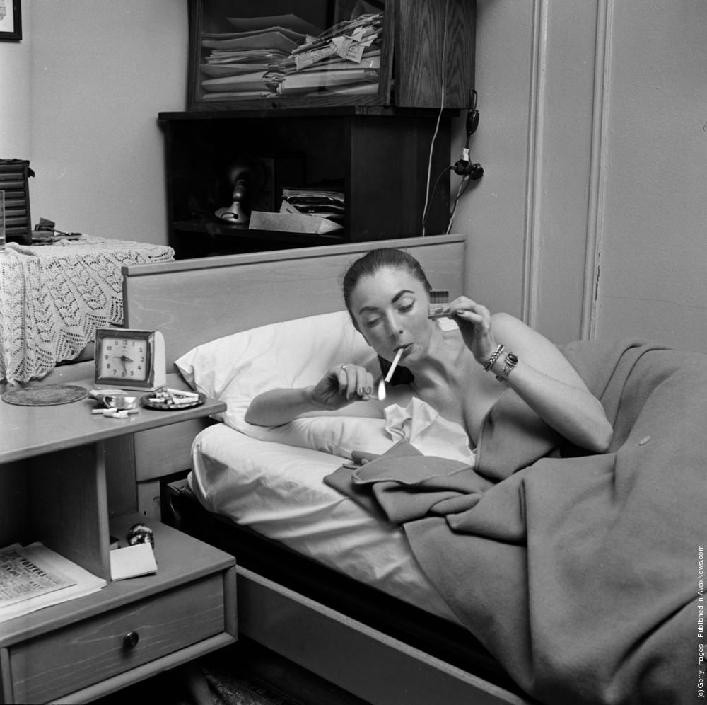 #13 A member of a teenage girl gang lying in bed smoking a cigarette, circa 1955.