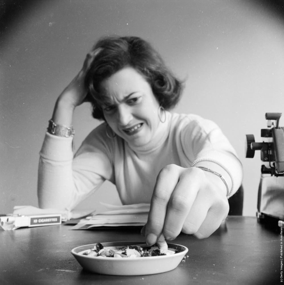 #14 An office worker leaves her typewriter for a moment for a smoke, and anxiously crushes out another cigarette into an already full ashtray, 1955.