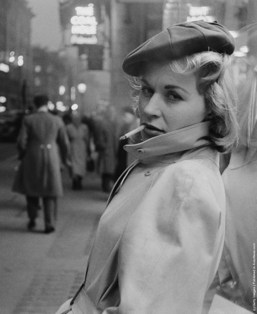 #19 Austrian actress Julia Arnall, leaning against a shop window and smoking a cigarette. 27th February 1956.