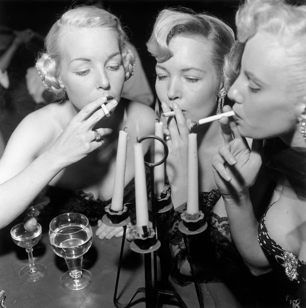 #27 Three aspiring actors Shirley Buchanan, Mara Lynn, and Donna Williams light their cigarettes from a candelabra at a bar, Loreto, Mexico, 1950s.