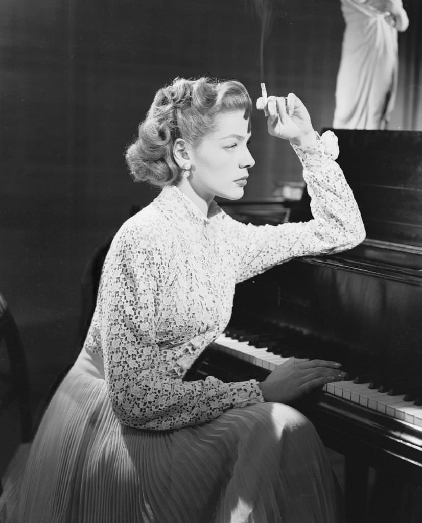#28 American screen star Lauren Bacall smoking, sits thoughtfully at the piano for the film ‘Young Man With A Horn,’ 1950.