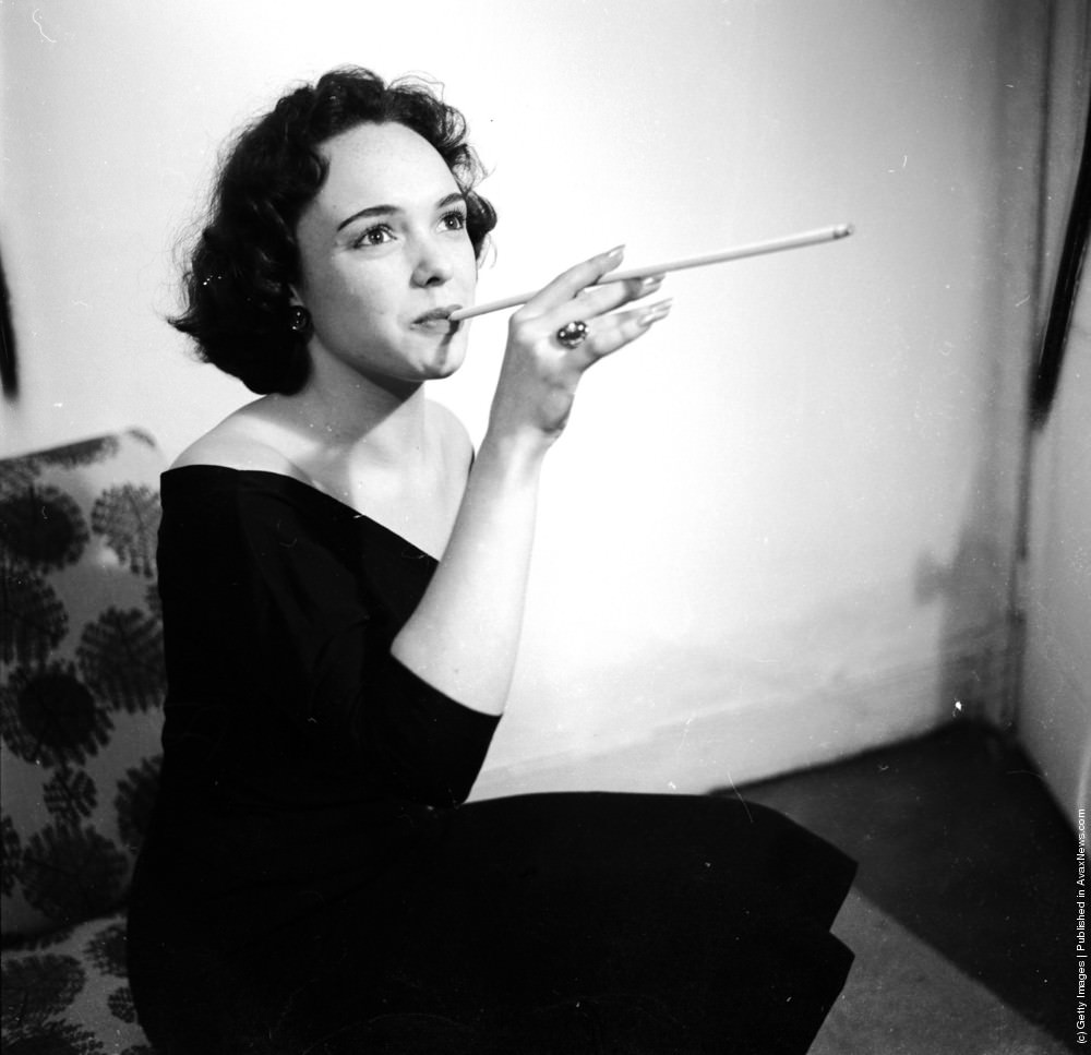 #6 A woman smoking a long cigarette which she has constructed using a rolling machine. April 1953.