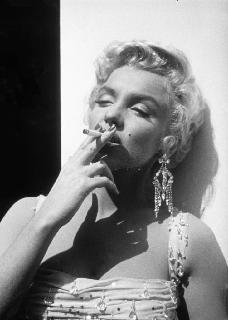 #52 Marilyn Monroe smoking a cigarette on the set of “There’s No Business Like Show Business,” 1954.