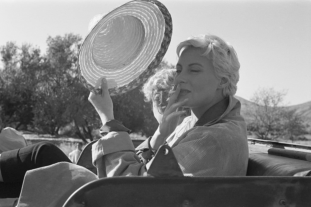 #62 Shooting of the film ‘Oasis’ by Yves Allegret in Morocco: Michèle Morgan smoking a cigarette in a jeep next to Cornell Borchers, 1955.