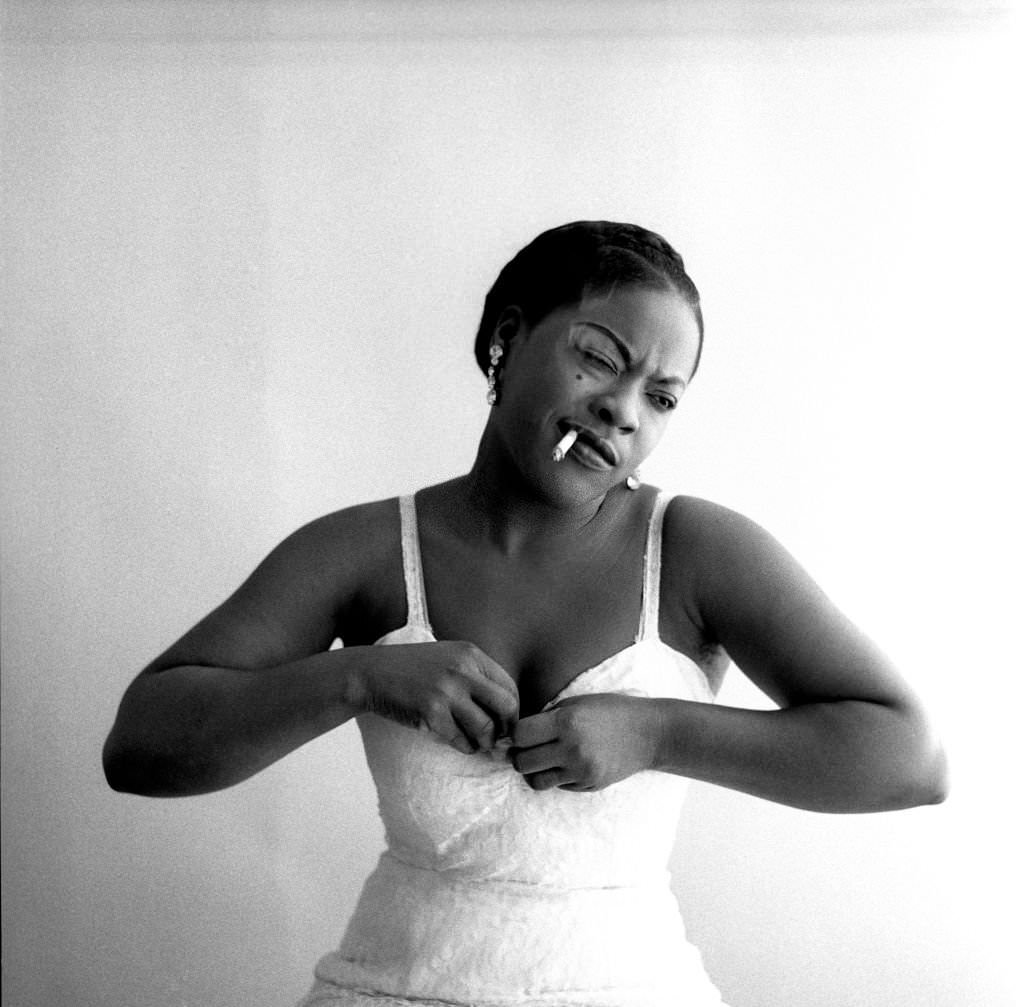 #84 American singer LaVern Baker smoking and adjusting her dress in New York, New York, 1957.