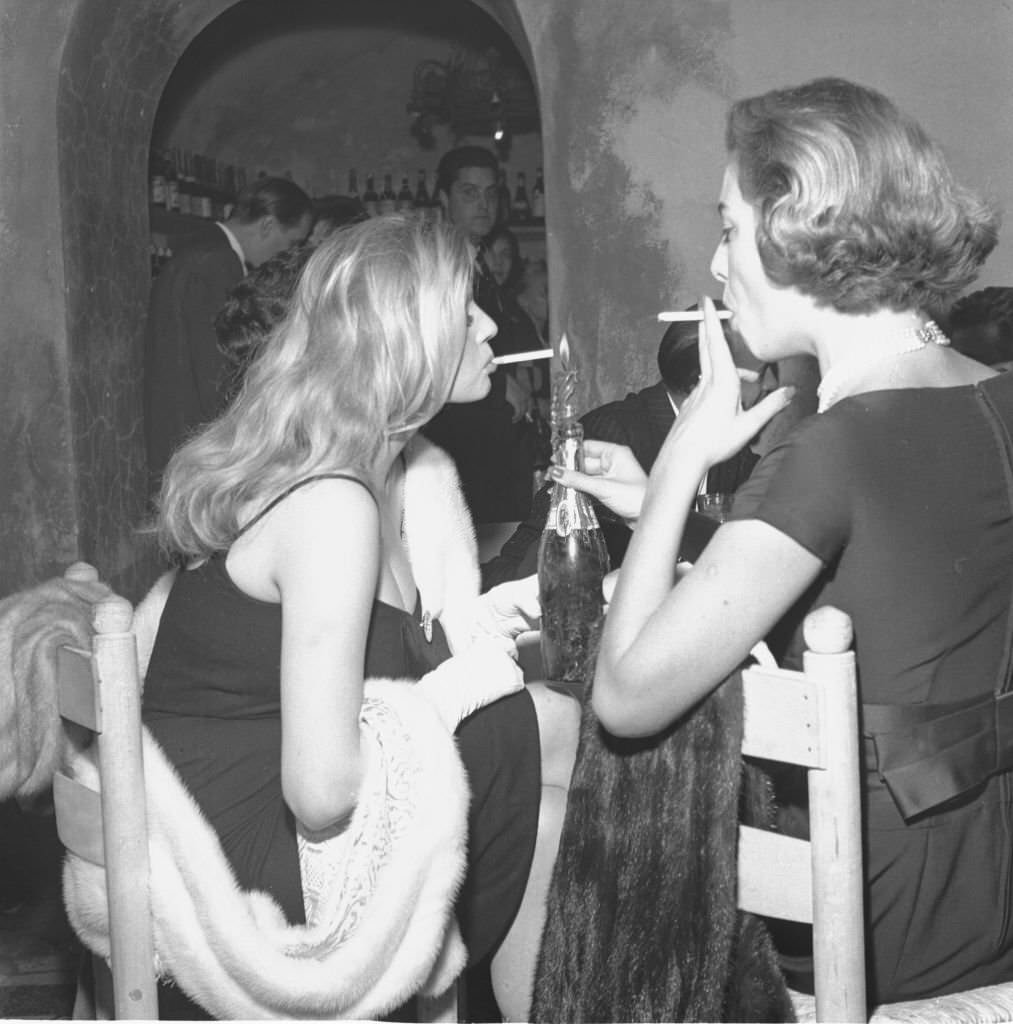 #86 Actress Anita Ekberg smokes a cigarette with Gaea Pallavicini at a dinner party in Rome, 1958.