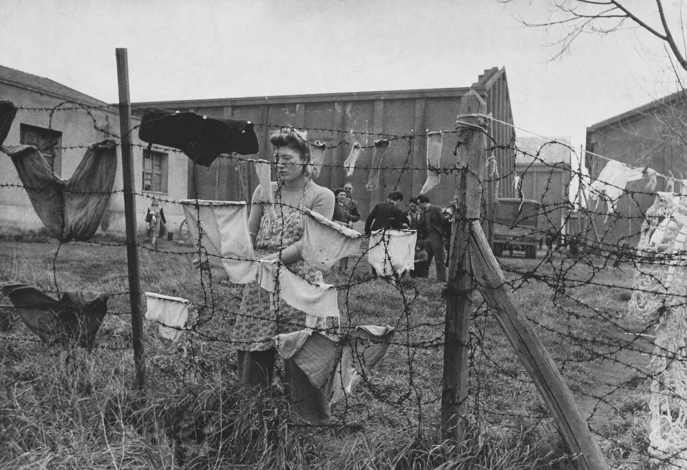 #16 Italian Woman Refugee Hangs Laundry on Barbed Wire Fence in Rome, Year Unspecified