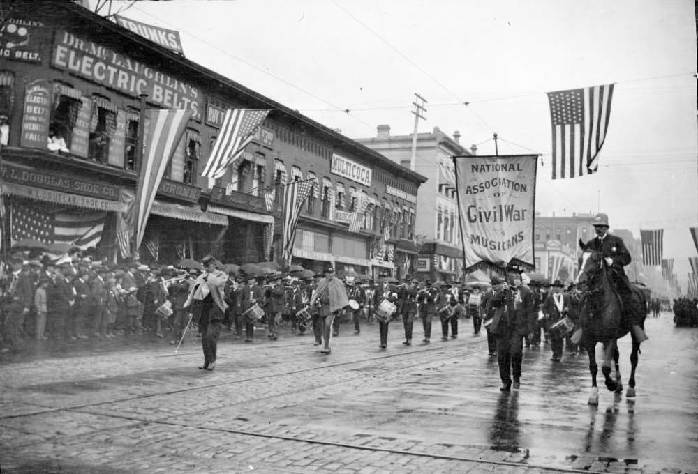 #87 Parade on 17th Street, Denver with marching band, spectators, and signs on buildings for various businesses, 1900s