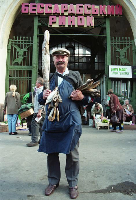 #53 Man with Fish: Vendor proudly displays assorted dried fish at a large market