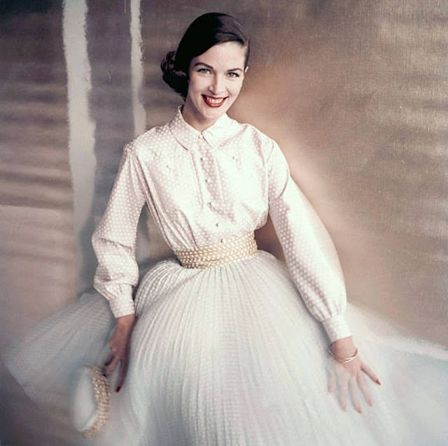 #21 Theo Graham wears a pale pink shirt and pleated blue skirt with white dots, accented by a yellow dotted cummerbund, 1955.