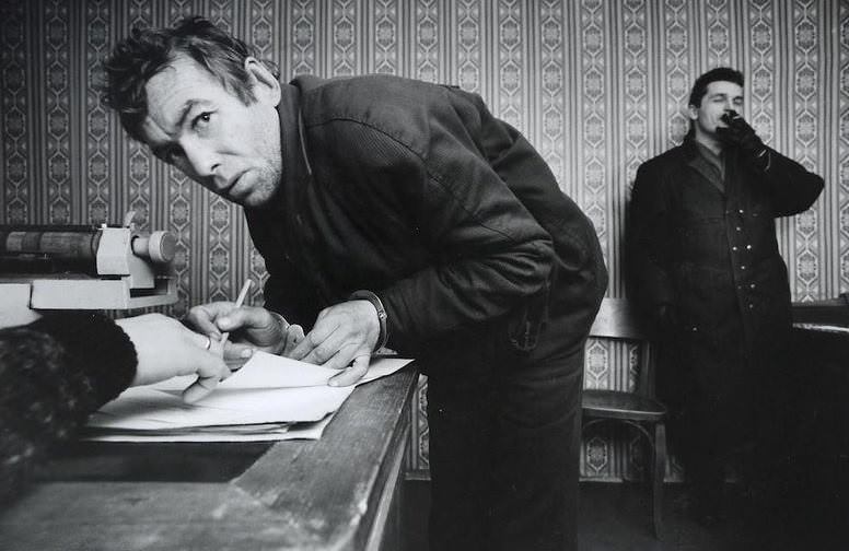 #31 A petty thief signing his confession at the local police station, December 1992. The arresting officer stands in the background.