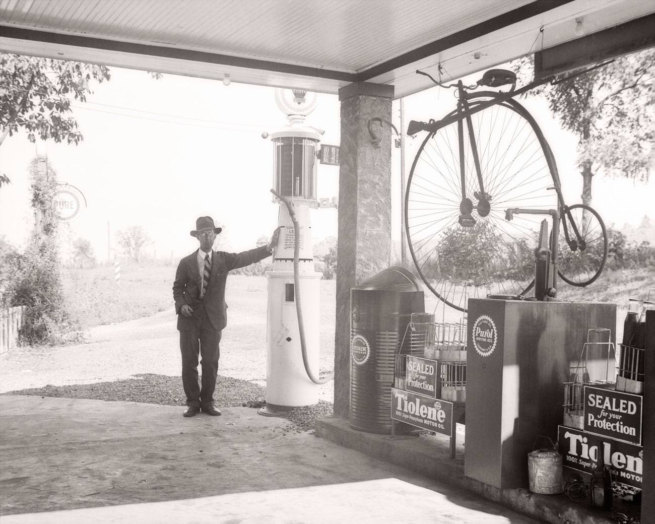 #17 Man leaning on gas pump at filling station in Ohio with antique displays, 1940s.