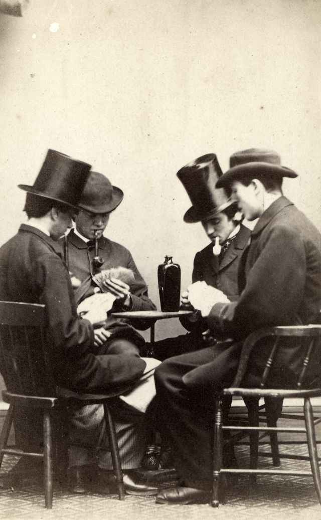 #25 Four gentlemen with pipes clenched in their teeth sit with playing cards and a bottle of gin
