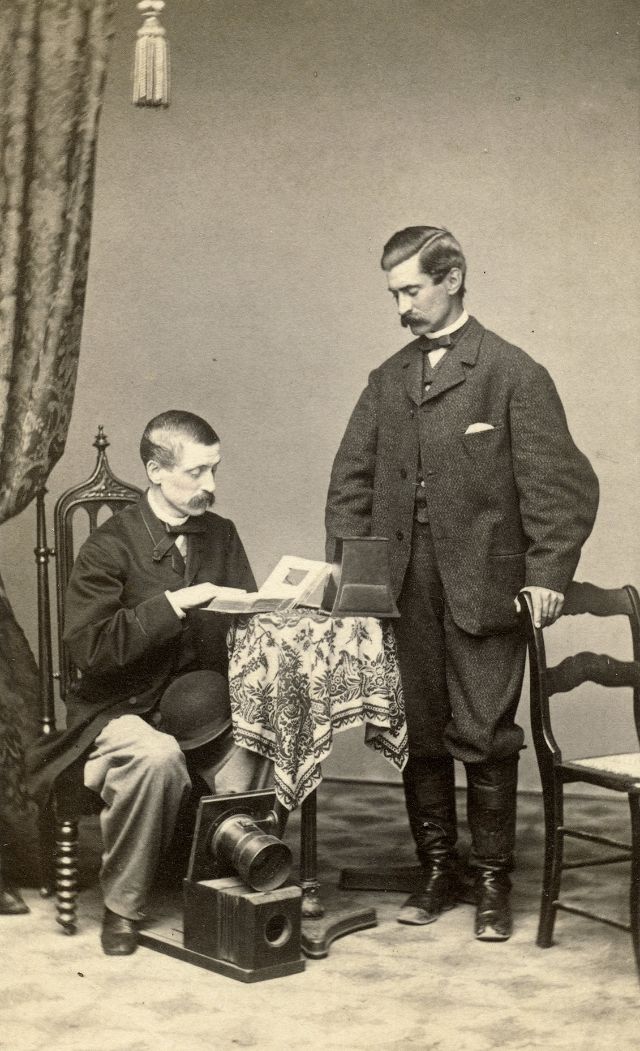 #38 Two gents pose with a wet plate camera equipped with a Petzval lens, a carte de visite album and a stereoviewer