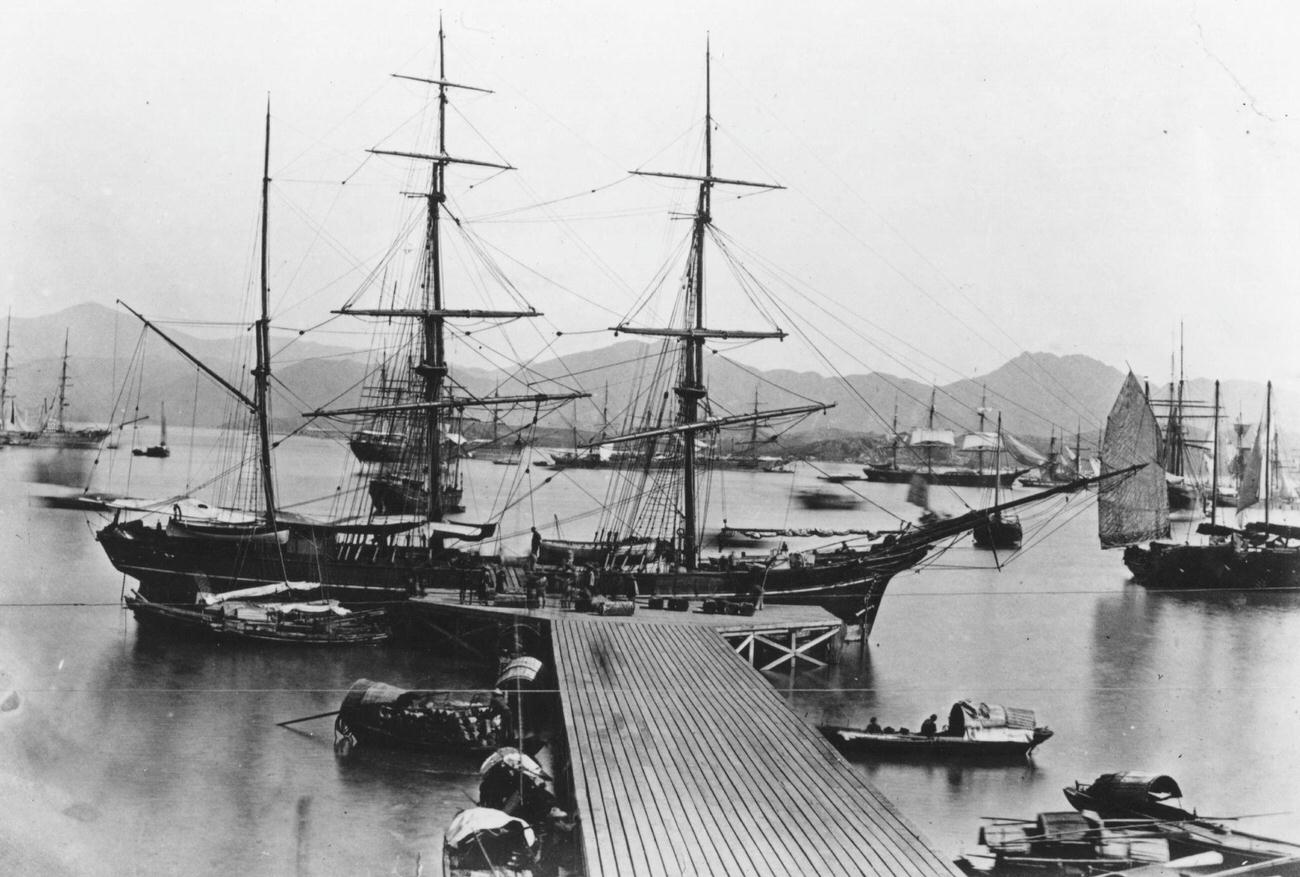 #64 A sailing ship docked at a jetty in Hong Kong harbor, surrounded by other boats, circa 1860.