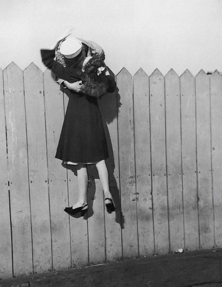 #16 Sailor lifting girlfriend for a kiss over fence, 1945.