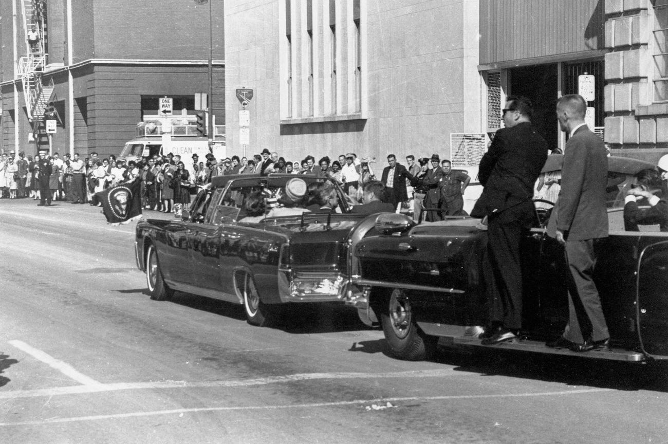 #14 John F. Kennedy’s motorcade passes the Texas School Book Depository in Dallas, Texas, before the assassination, 1963.