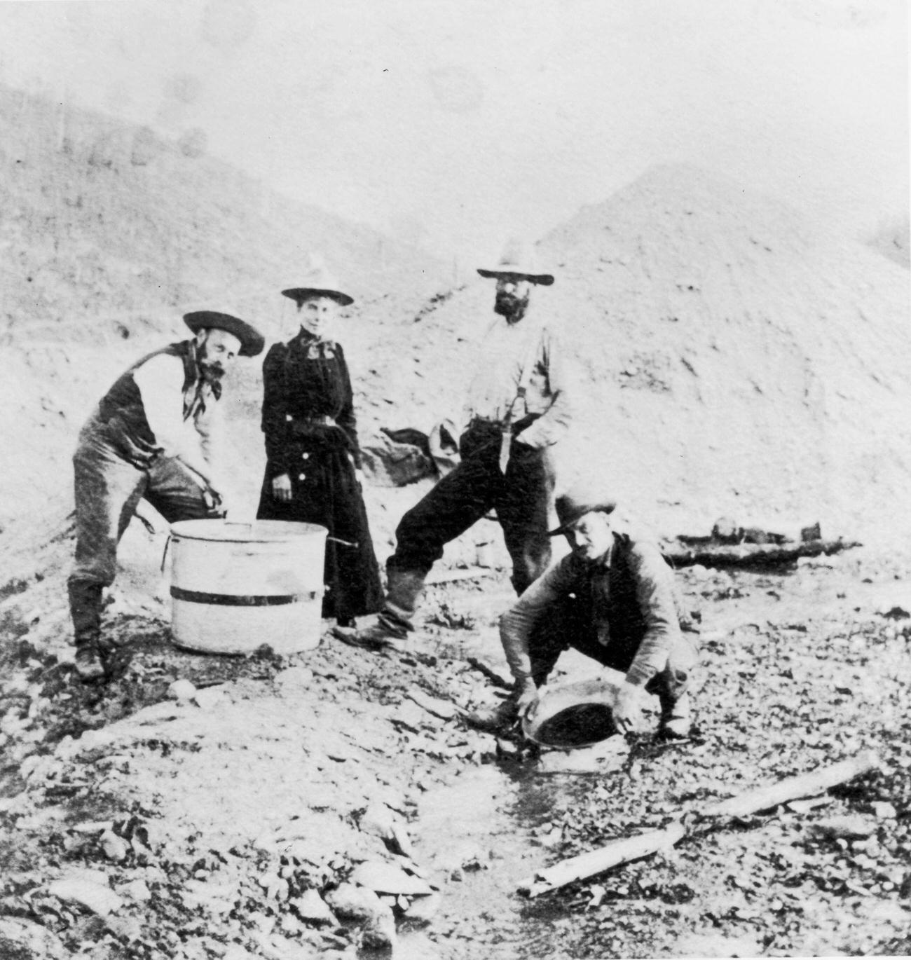 #15 Three men and a woman panning for gold in a riverbed during the Klondike Gold Rush, Alaska.