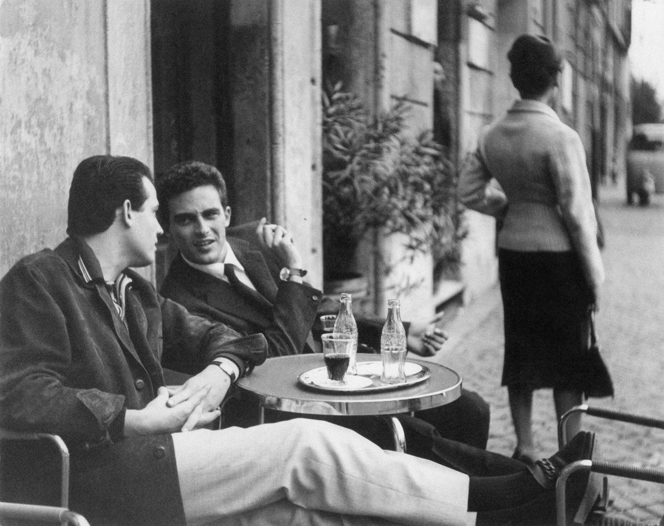 #79 Two men chatting at a café table with Coca-Cola bottles, 1959.
