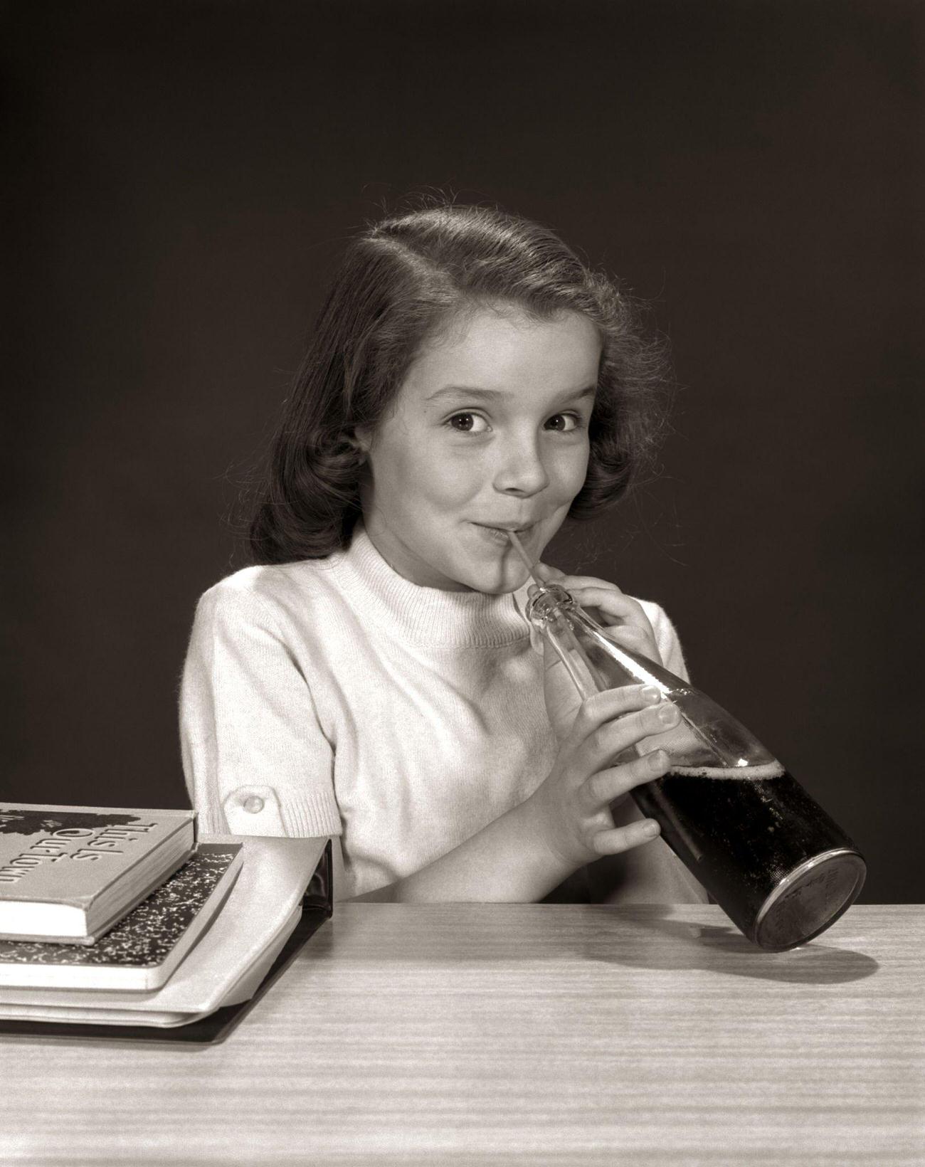 #96 Smiling school girl drinking a carbonated beverage from a bottle, 1950s
