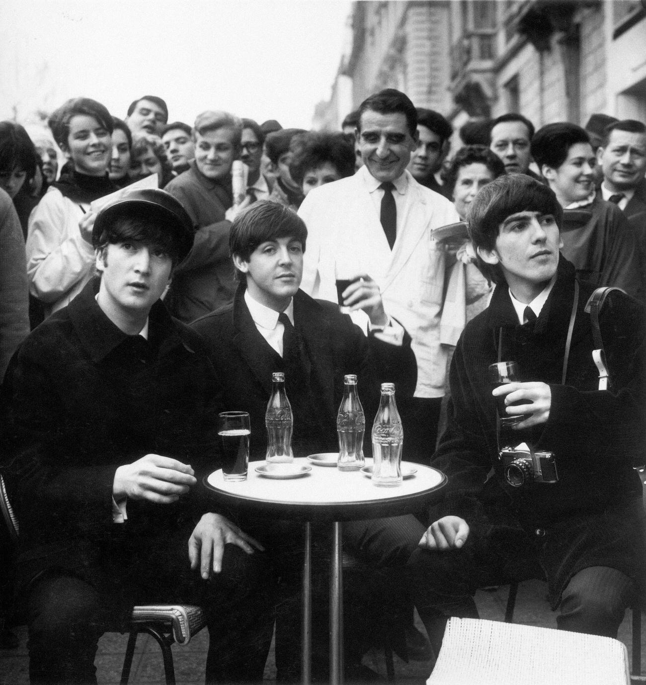 #98 Beatles John, Paul, and George enjoying Coca-Cola at a cafe in Paris1964.