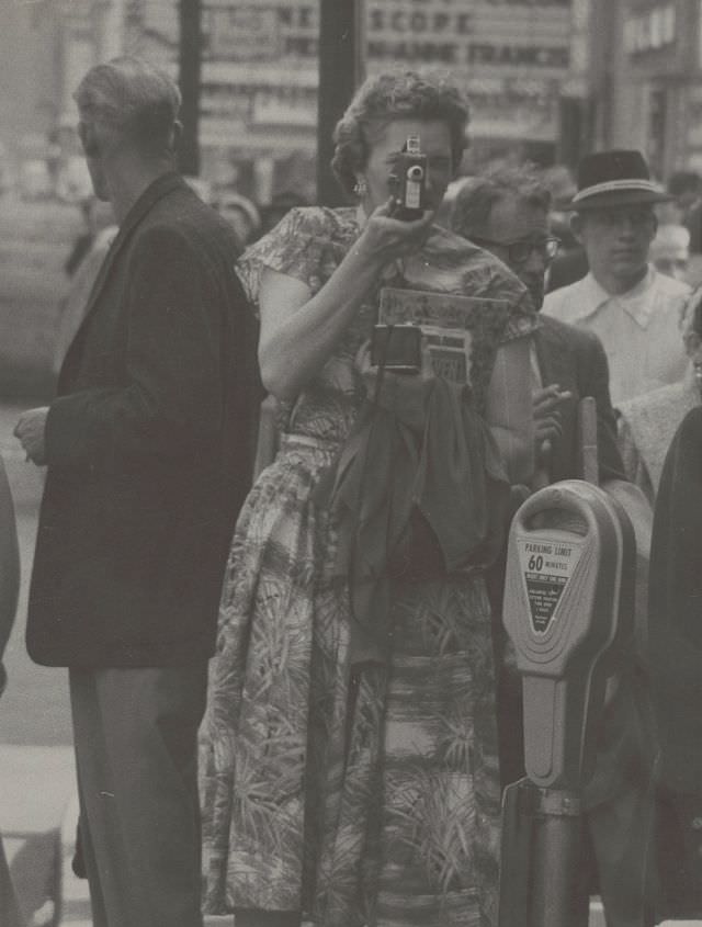 #18 Woman holding a home movie camera while walking on New York City sidewalk, 1956