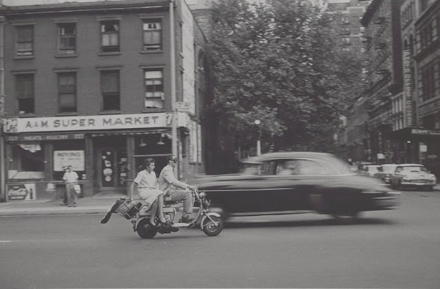 #21 View of man and woman on motorized scooter, A&M Super Market in back, September 1957