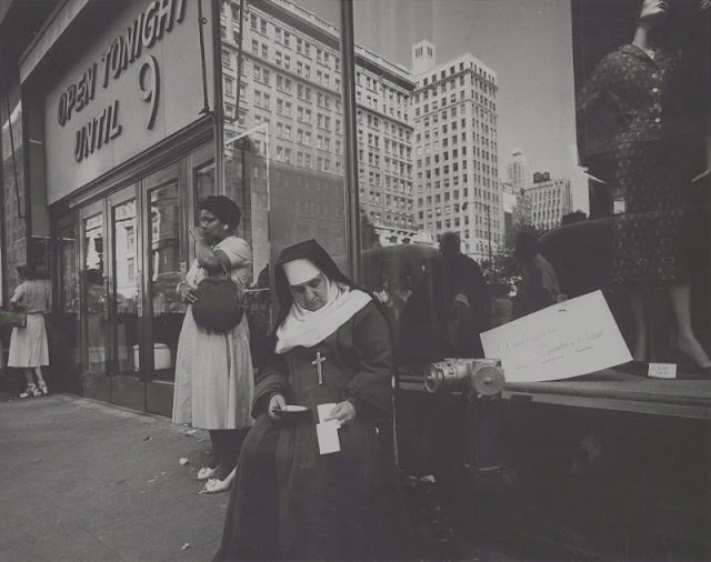 #26 Nun sitting in front of a store window, August 1958