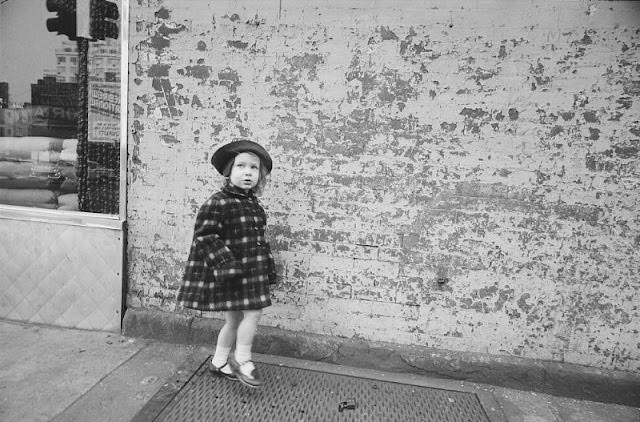 #31 Little girl walking on sidewalk cellar hatch doors looking warily at the photographer, March 1959