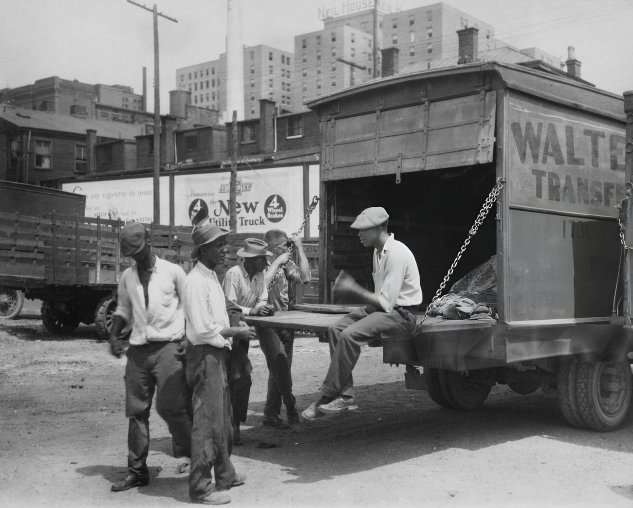 #1 A group of men playing craps, one sitting on a truck’s tailgate, at a transport facility on the banks of the Scioto River with the Neil House hotel in the background, Columbus, Ohio.