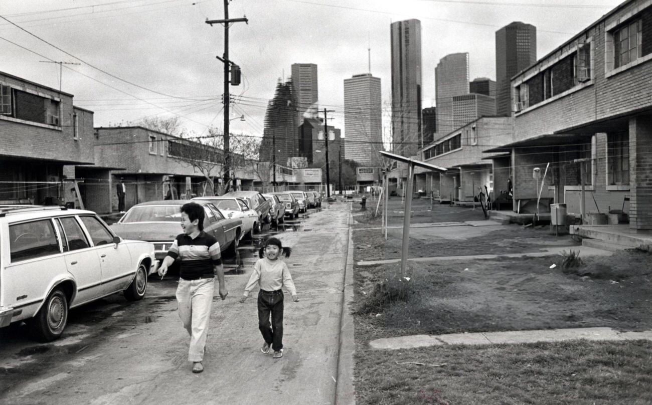 #54 Sinh Thang and Anh Bich Tin walk between rows of apartments in Allen Parkway Village, Houston, Texas, 1983.