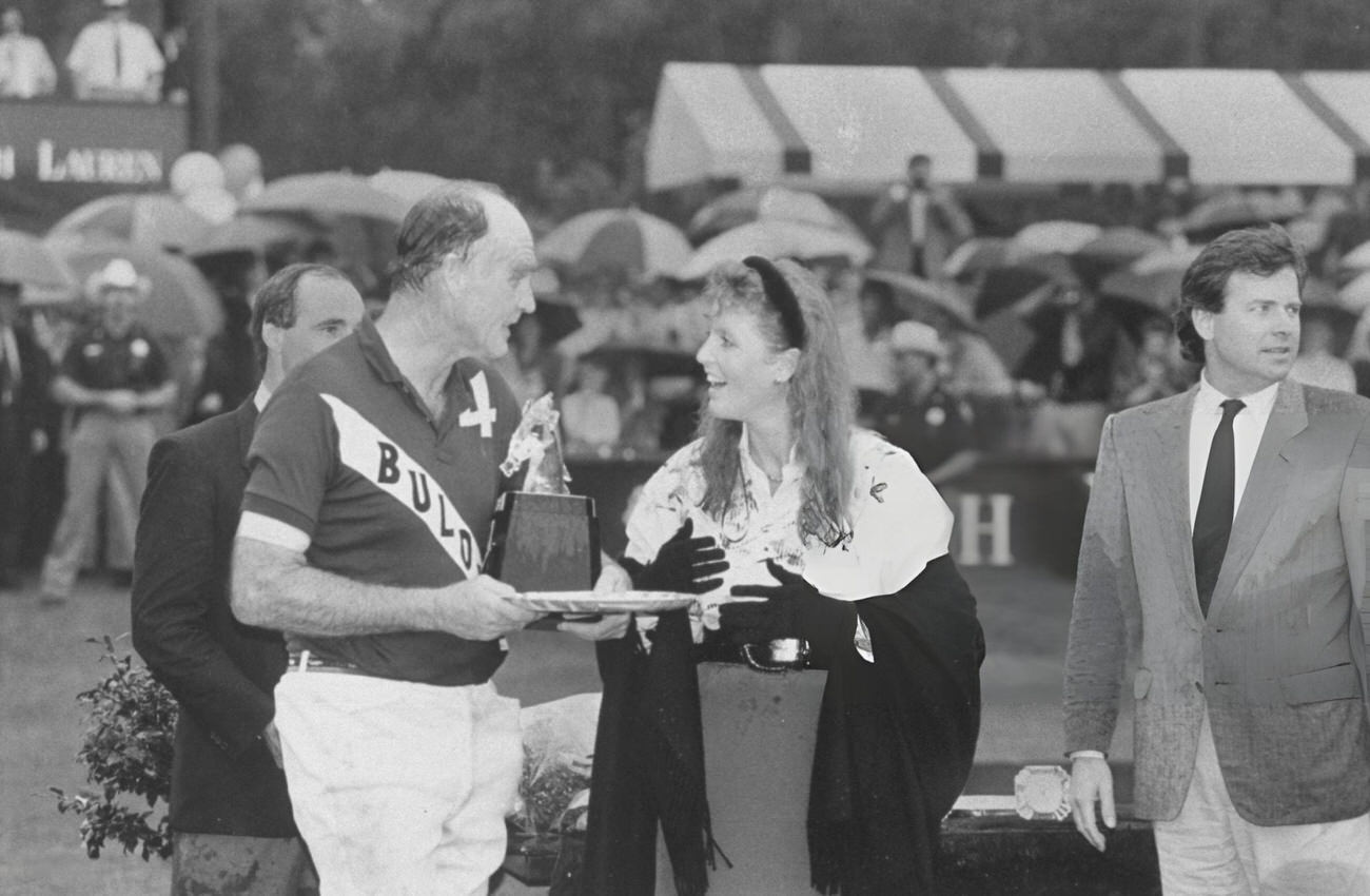 #90 Sarah Ferguson stands in the rain on a polo field with her father, Major Ronald Ferguson, during her visit to Houston, Texas.