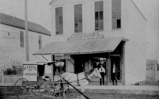 #21 Bakery and Groceries building with two men posing, 1880s