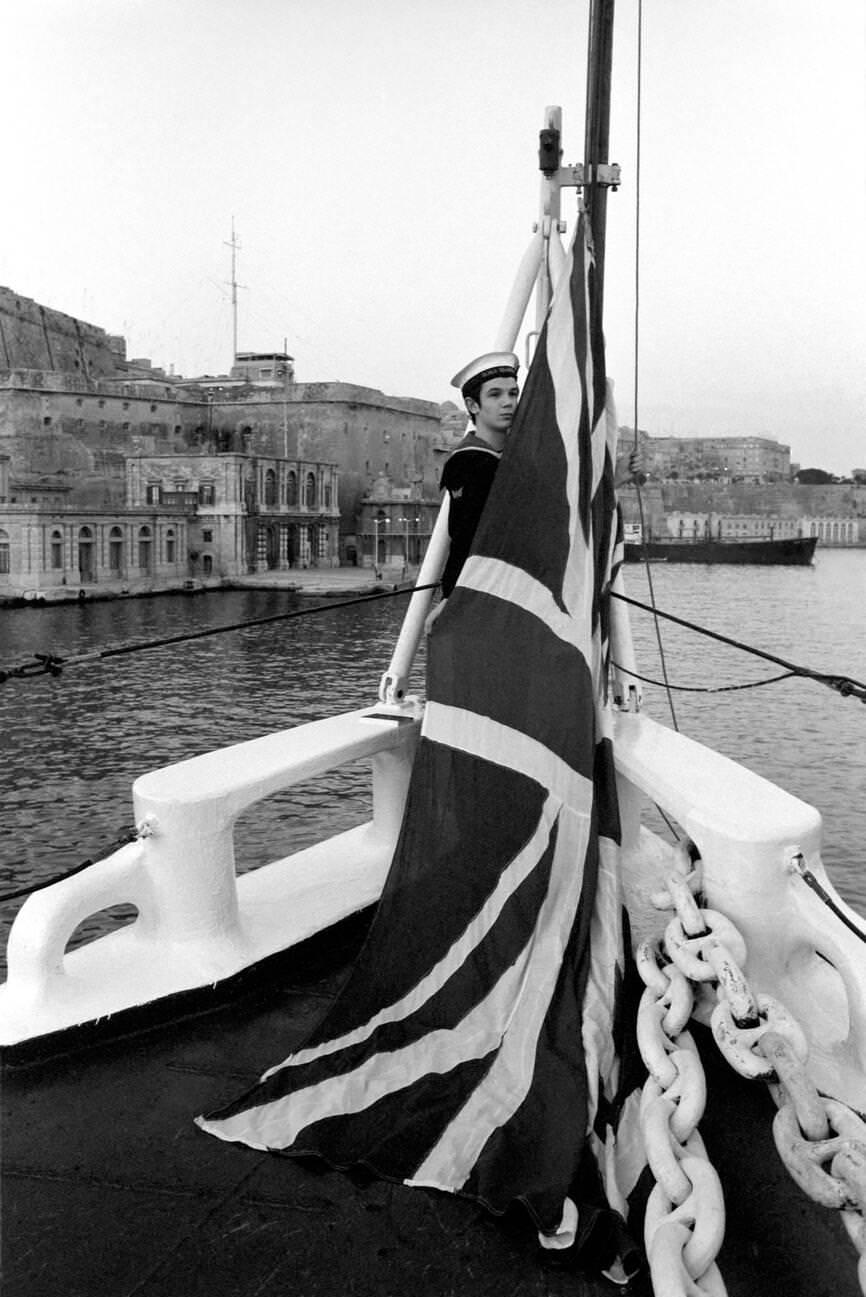 #70 Radio operator Brian Houston covers the Union Jack at sunset in H.M.S. Blake in Valletta, Malta, 1972.