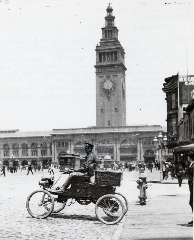 #133 Lester L. Whitman at the tiller of a Curved Dash Olds Light Runabout in front of the Ferry Building, July 6, 1903
