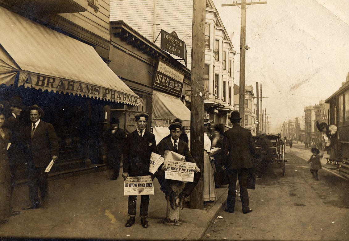 #24 Pete Rielly and Eddie Campi selling newspapers in front of Abraham’s Pharmacy, 1198 McAllister Street, at Fillmore, 1909.