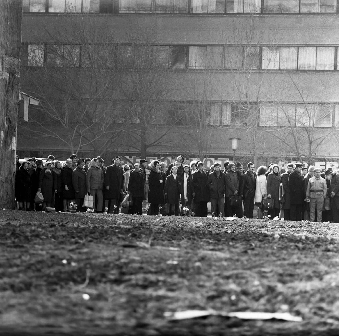 #33 People in line for groceries with flowers for earthquake victims in Bucharest, Romania, March 1977.