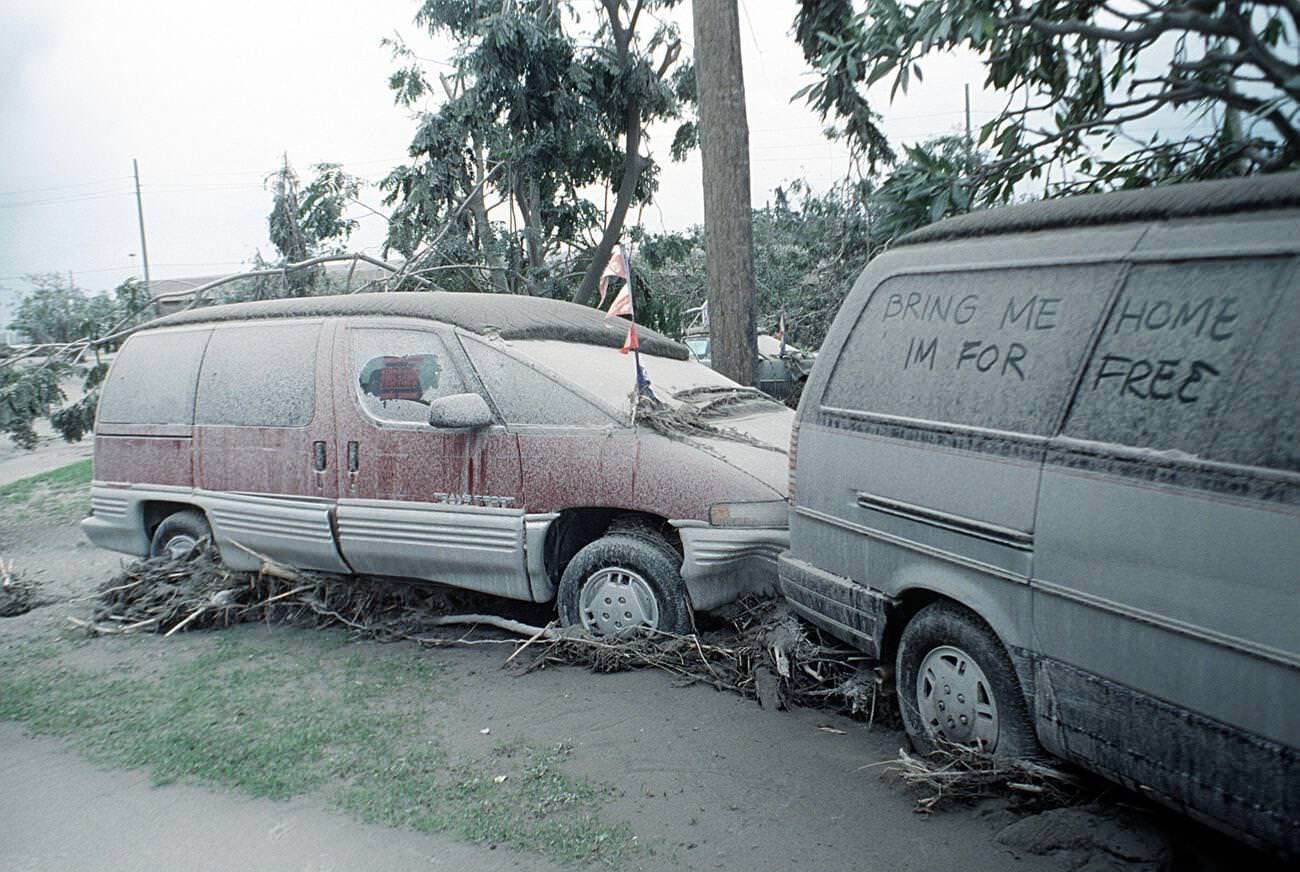 Two vehicles covered in volcanic ash in a lot at Clark Air Base, Luzon