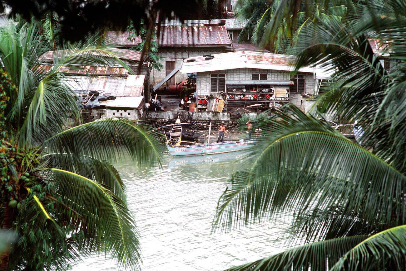 #45 Houses on a riverbank in the Philippines, framed by palm trees, 1981.