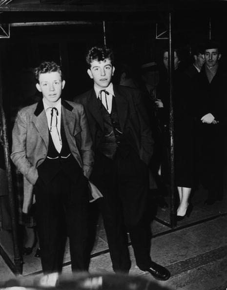 #11 Two original 1954 Teddy Boys at Kingston upon Thames wearing Drape Jackets with 4″ wide lapels, silk patterned waistcoats and trousers with pleated fronts and 16″ bottoms with turn-ups.