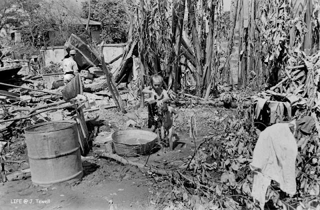 #49 Older Filipino woman giving a child a bath by the ruins of her home, Manila, Philippines, March 1945